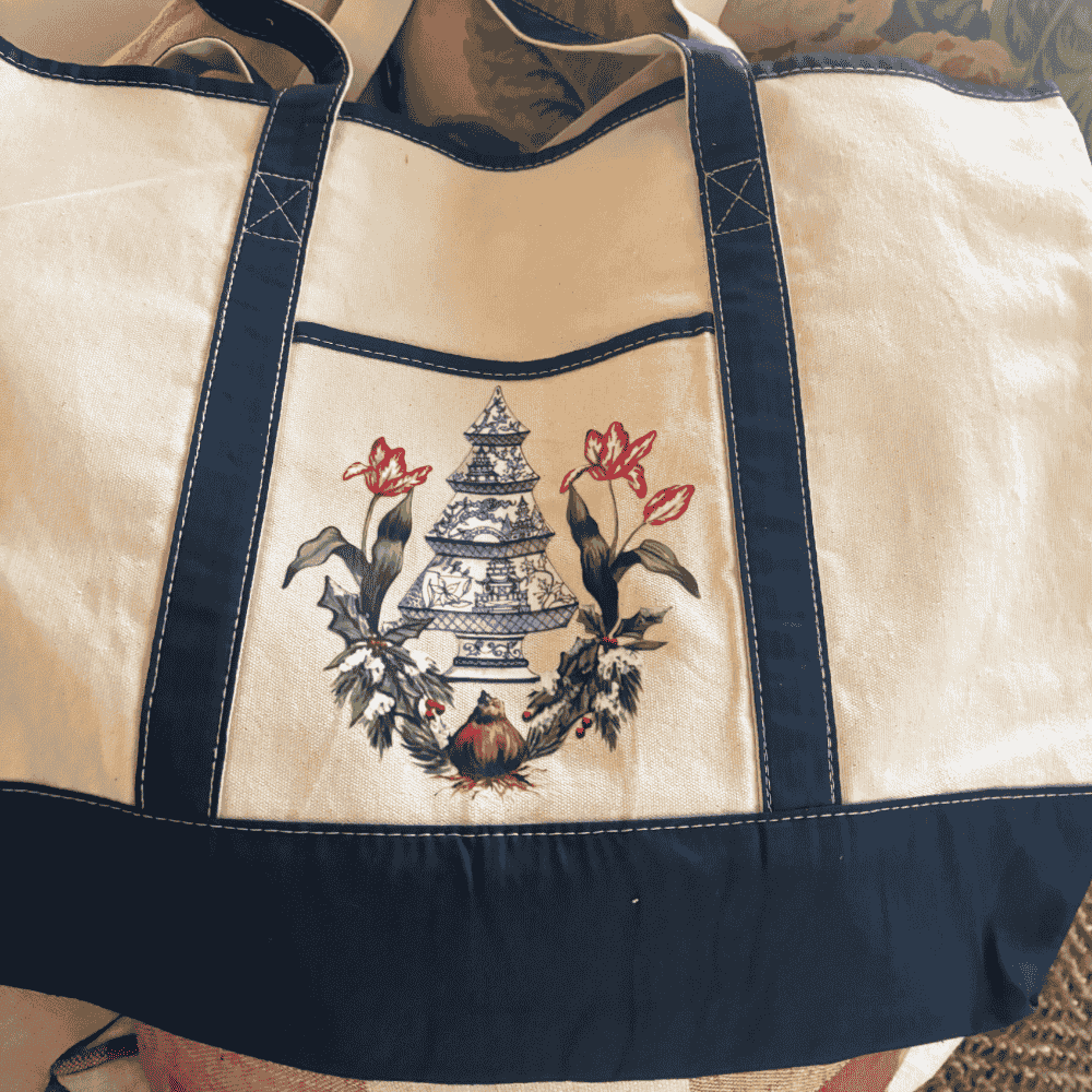 Canvas tote with navy straps and trim, featuring a beautifully detailed blue and white porcelain pagoda tree surrounded by festive holly and two red tulips sprouting from a bulb.