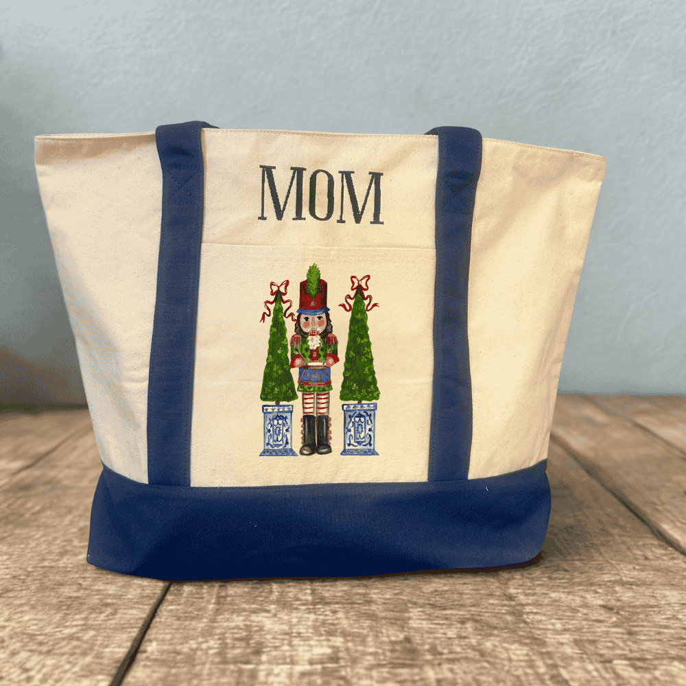 Monogrammed holiday canvas tote with “MOM” above a nutcracker and topiary design in festive red and green.