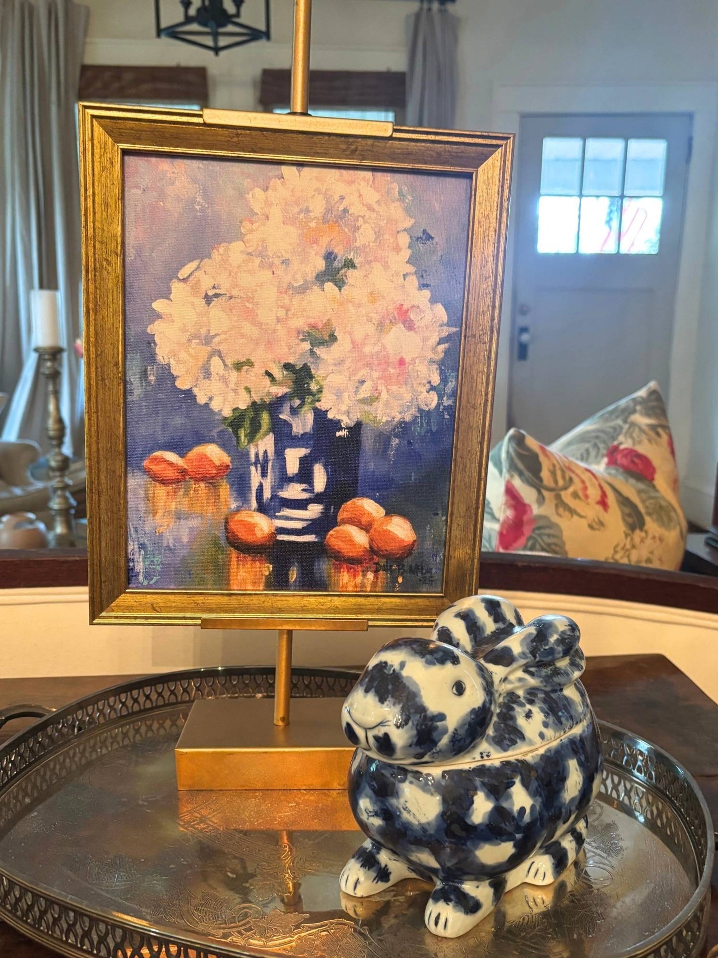 Photo of tabletop art featuring lush white hydrangeas in a cobalt blue vase surrounding by bright citrus fruit. It is framed in an antique gold finished frame and on a gold tabletop easel.