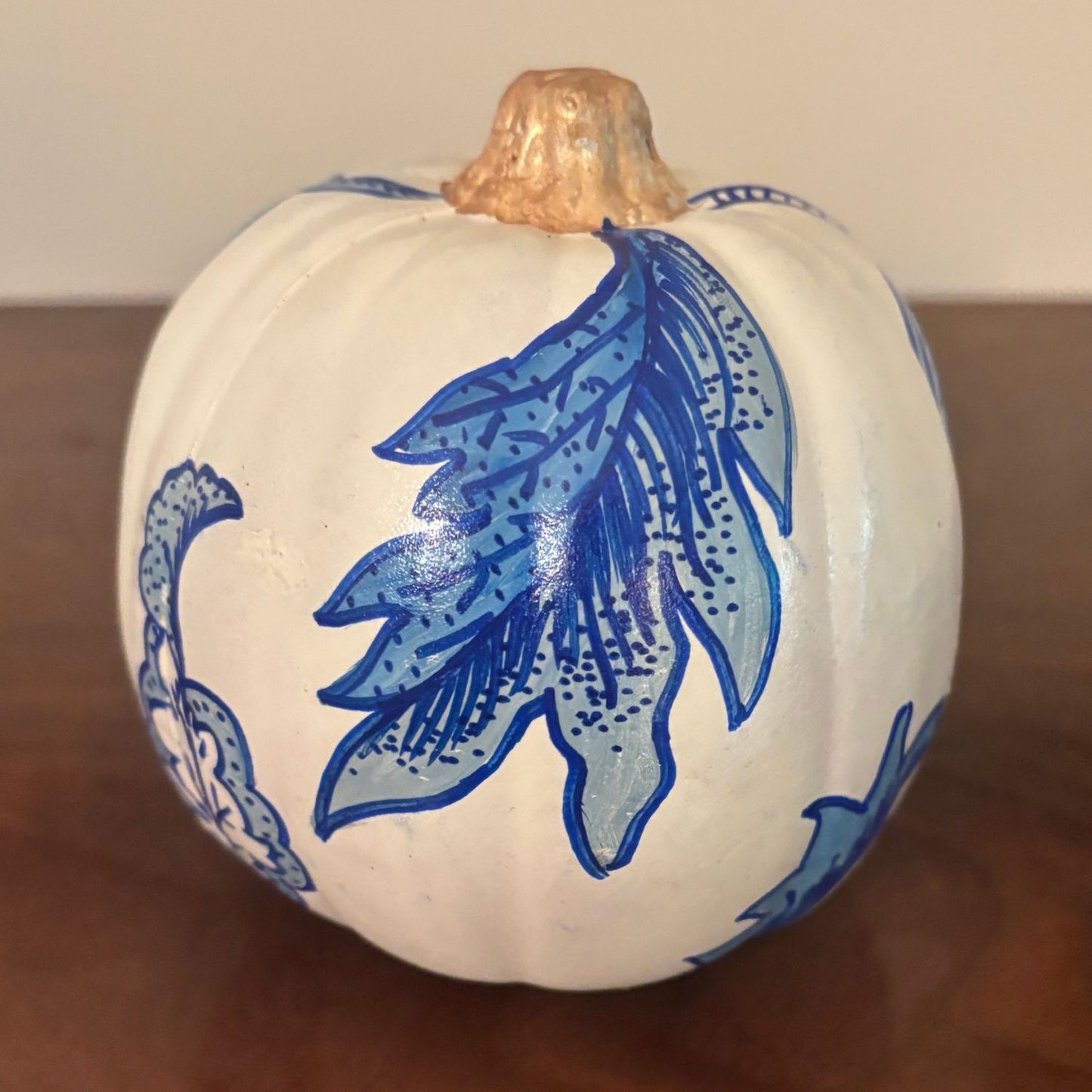 Close-up of detailed blue leaf motifs hand-painted on a white pumpkin with a metallic gold stem.