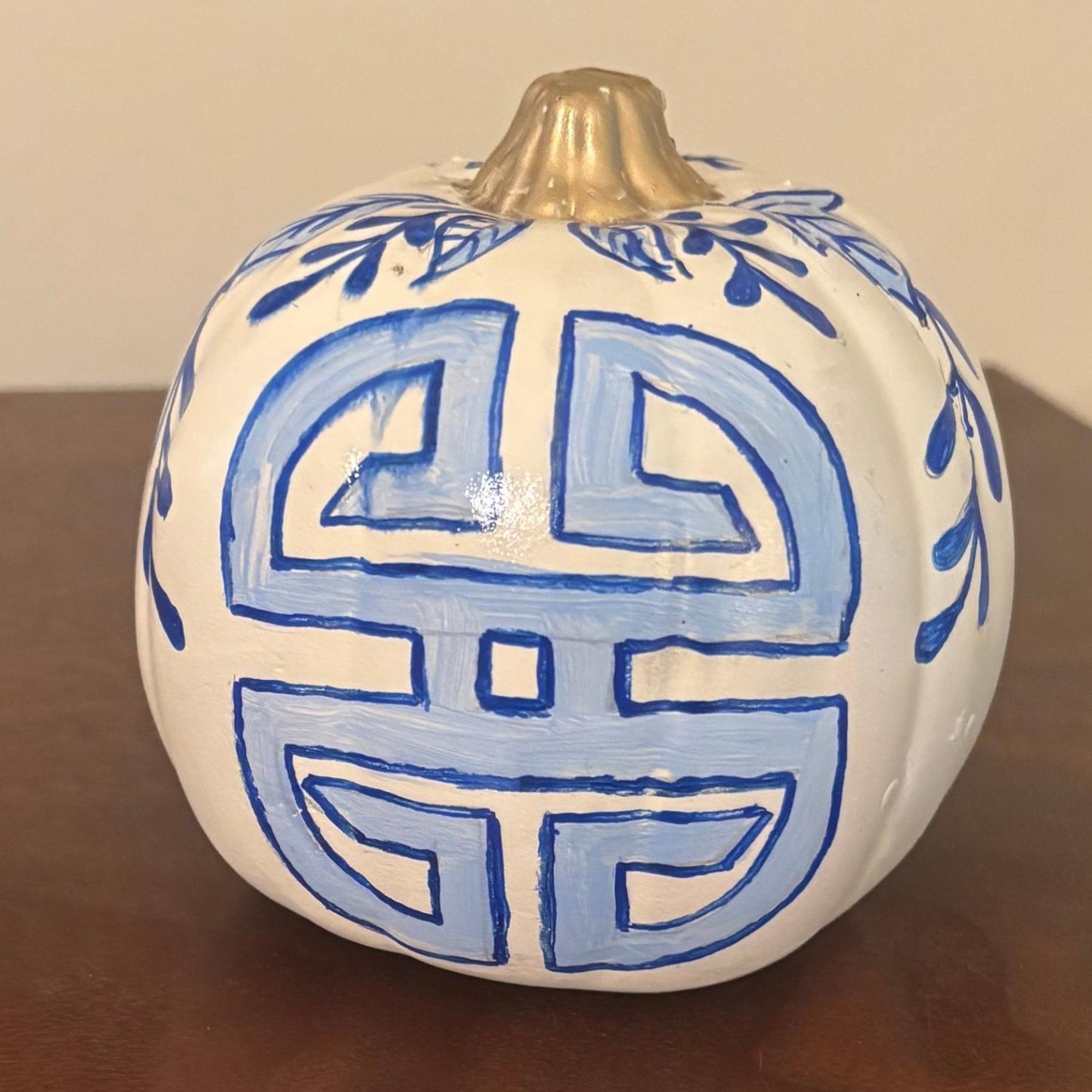 White pumpkin with a bold blue longevity symbol and leafy botanical details near the stem.