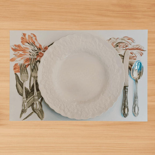Overhead photo of a fall harvest placemat featuring a vase with sunflowers, pumpkins, and apples with a cream colored plate and silverware on a wooden table
