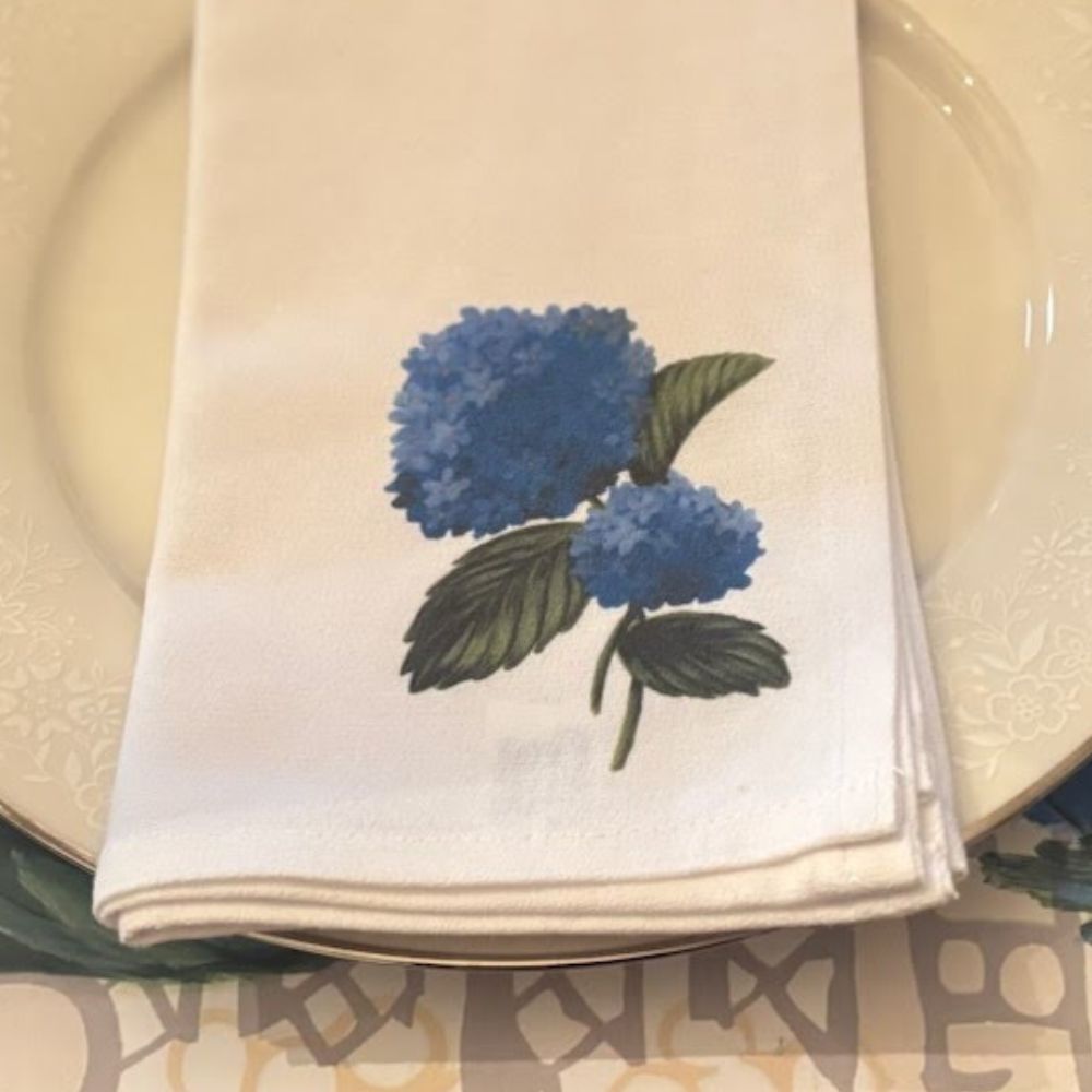 close up photo of a white cloth napkin with a blue hydrangea design