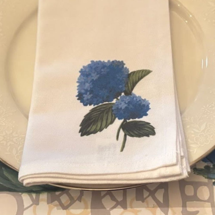 close up photo of a white cloth napkin with a blue hydrangea design