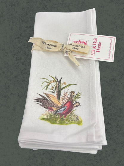 Folded cloth napkin with a vintage-style illustration of two pheasants and corn stalks, tied with a cream Hill & Dale Home ribbon and tag.