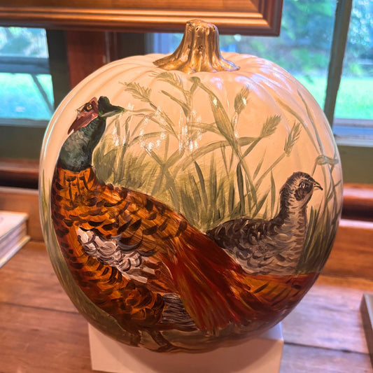 Hand-painted pumpkin featuring a colorful male pheasant in a grassy field, displayed on a wooden table with natural light.