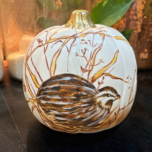 Hand-painted 6-inch decorative pumpkin featuring a nesting female quail nestled in tall autumn grasses, accented with gold and warm brown tones. The pumpkin has a soft cream base and a metallic gold stem, perfect for fall decor.