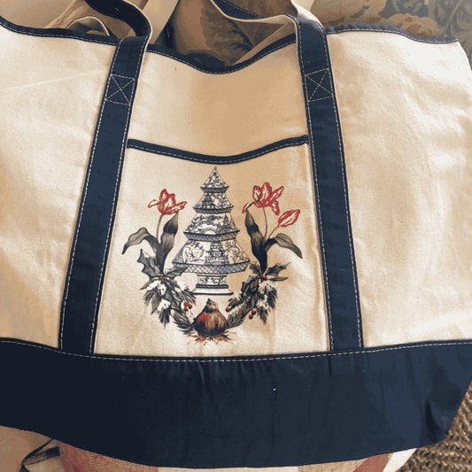 Canvas tote with navy straps and trim, featuring a beautifully detailed blue and white porcelain pagoda tree surrounded by festive holly and two red tulips sprouting from a bulb.