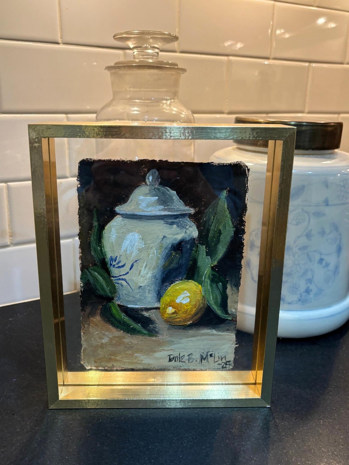 Hand-painted still life featuring a single lemon and classic porcelain jar, capturing a quiet Southern moment on textured Lokta paper, framed in a brass floating frame with clear glass for display.