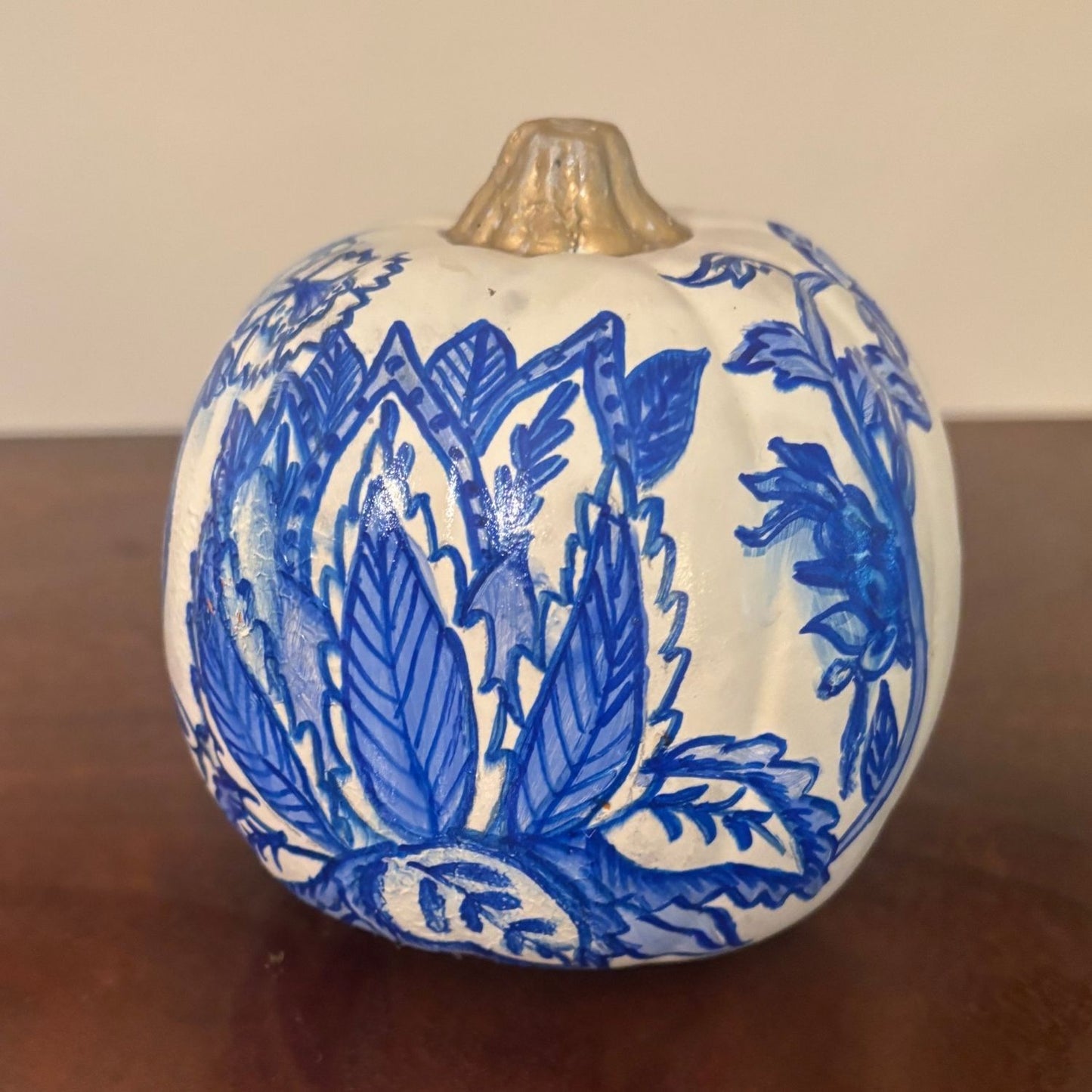 Close-up front view of the Lotus Bloom Pumpkin featuring hand-painted blue leaves in the shape of a lotus on a white background with a gold stem.