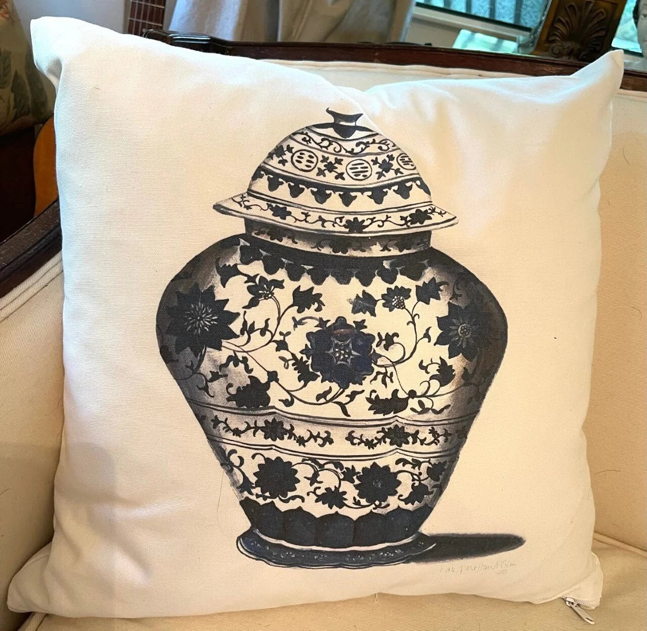 Photo of a square throw pillow with a blue chinoiserie floral vase design on a beige couch 