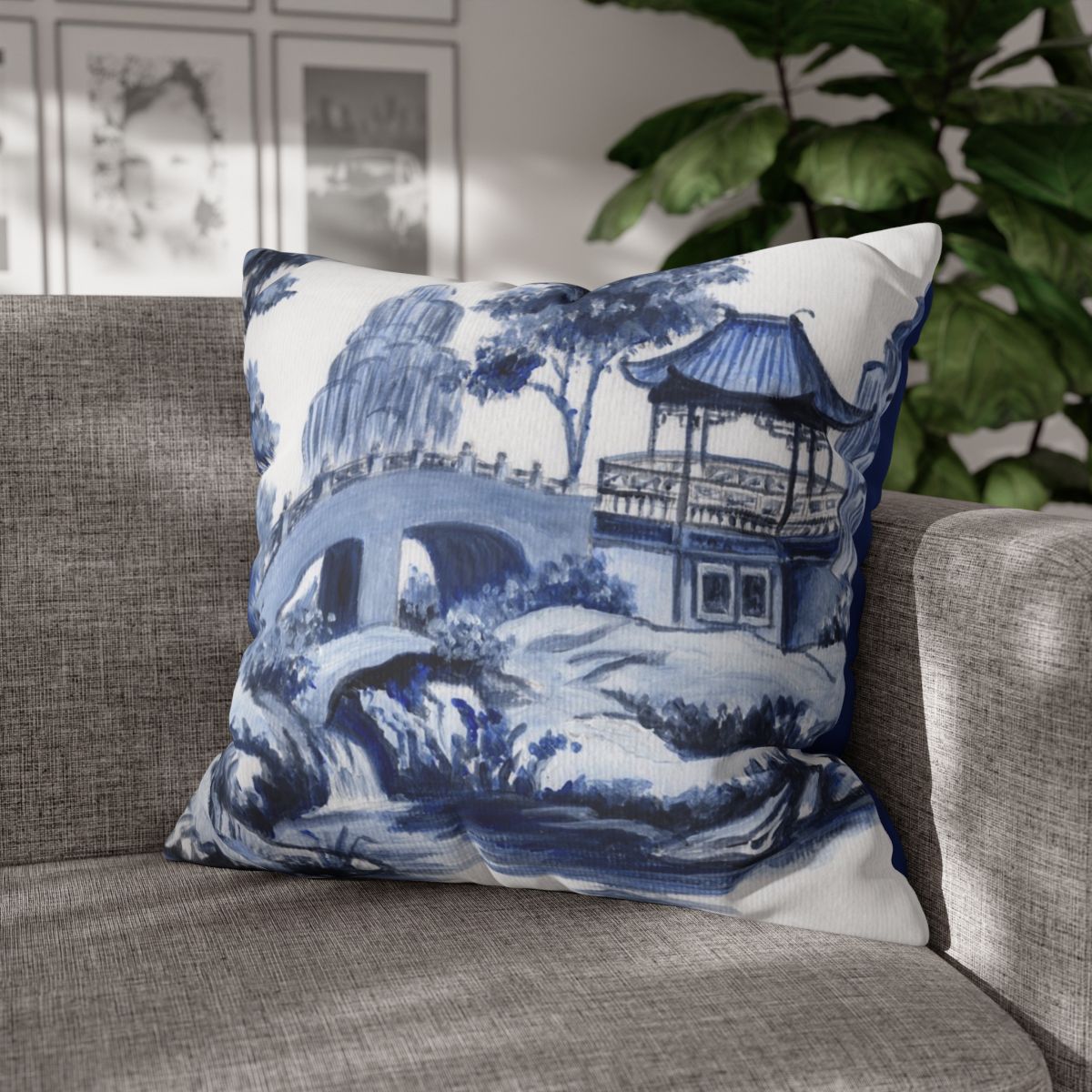 Photo of a throw pillow with a Chinoiserie pagoda scene in blue against a grey couch. 