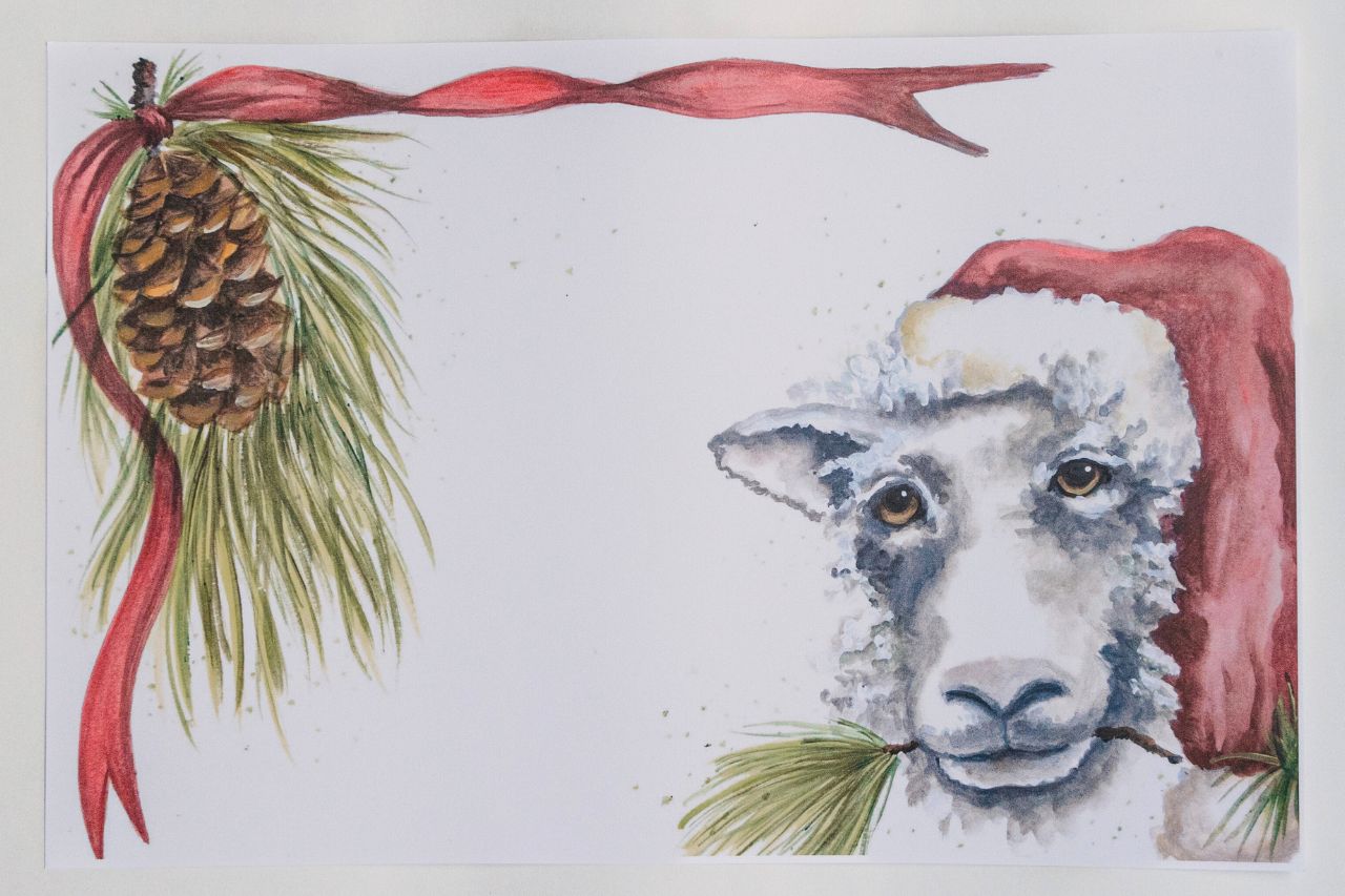 Photo of a holiday paper placemat against a white background. The artwork features a Santa hat-wearing sheep.