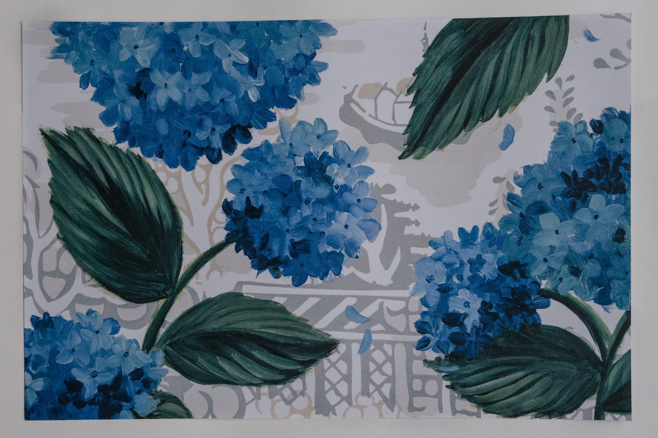 Photo of a paper placemat on a white background. The placemat features blue hydrangea artwork with a chinoiserie design in the background