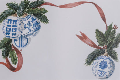 Up close photo of paper placemats featuring a placemats adorned with blue and white chinoiserie ornaments, festive greenery, and a bold red ribbon design