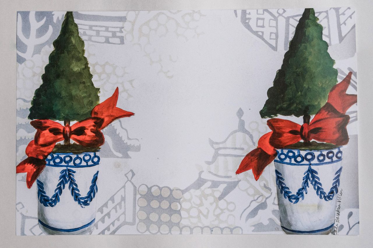 Photo of a paper placemat against a white background. The placemat features a Christmas topiary design against a chinoiserie background.