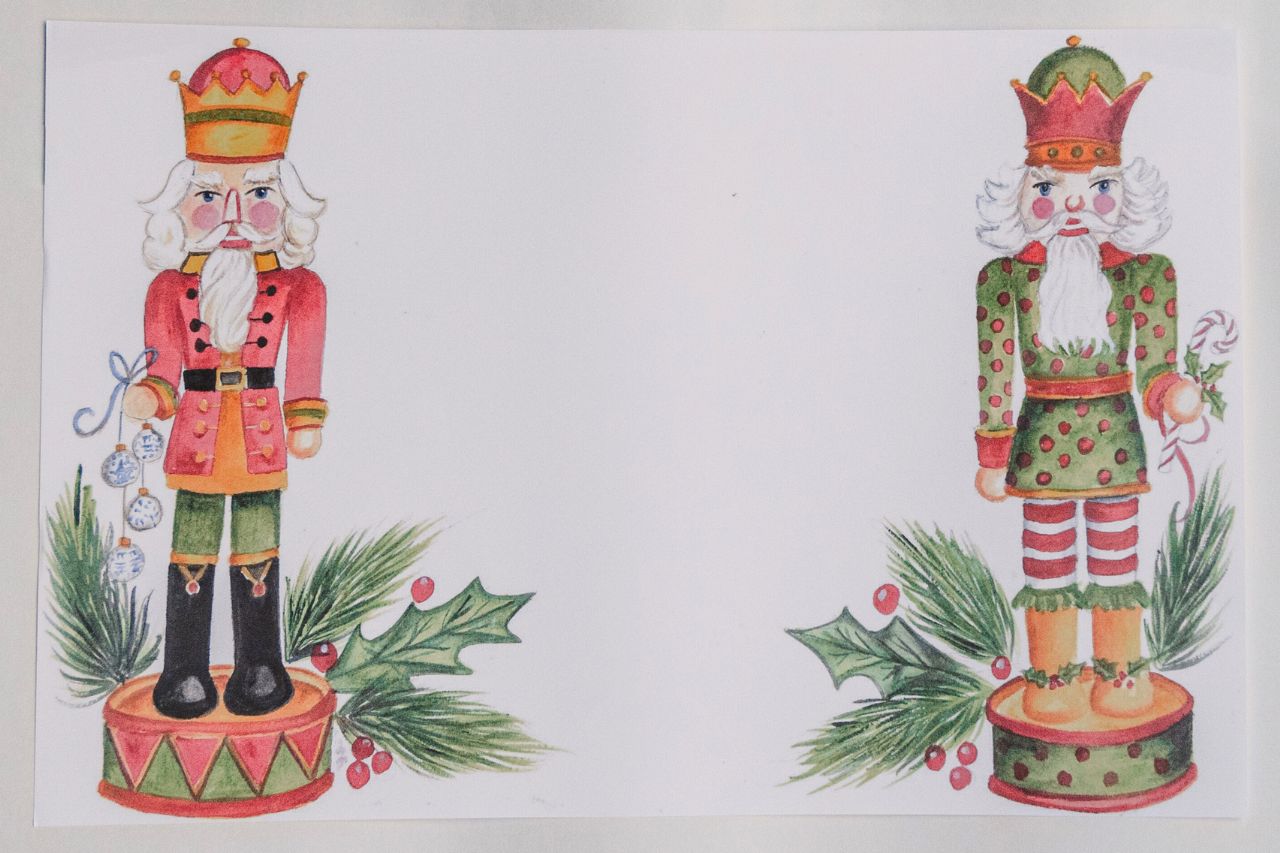 Photo of a paper placemat against a beige background. The artwork features two illustrated holiday nutcrackers