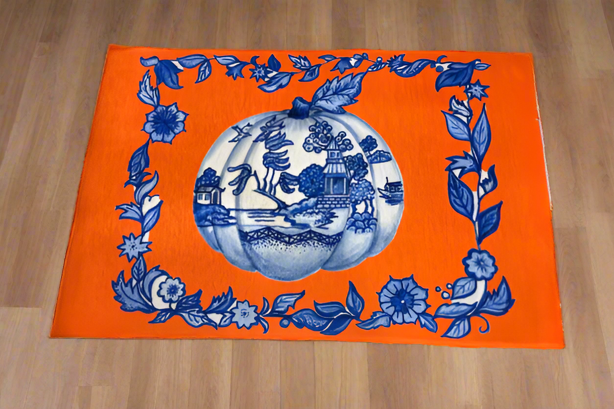 Photo of an orange rug with a chinoiserie painted pumpkin and blue flower artwork border on a hardwood floor