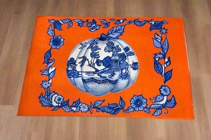 Photo of an orange rug with a chinoiserie painted pumpkin and blue flower artwork border on a hardwood floor