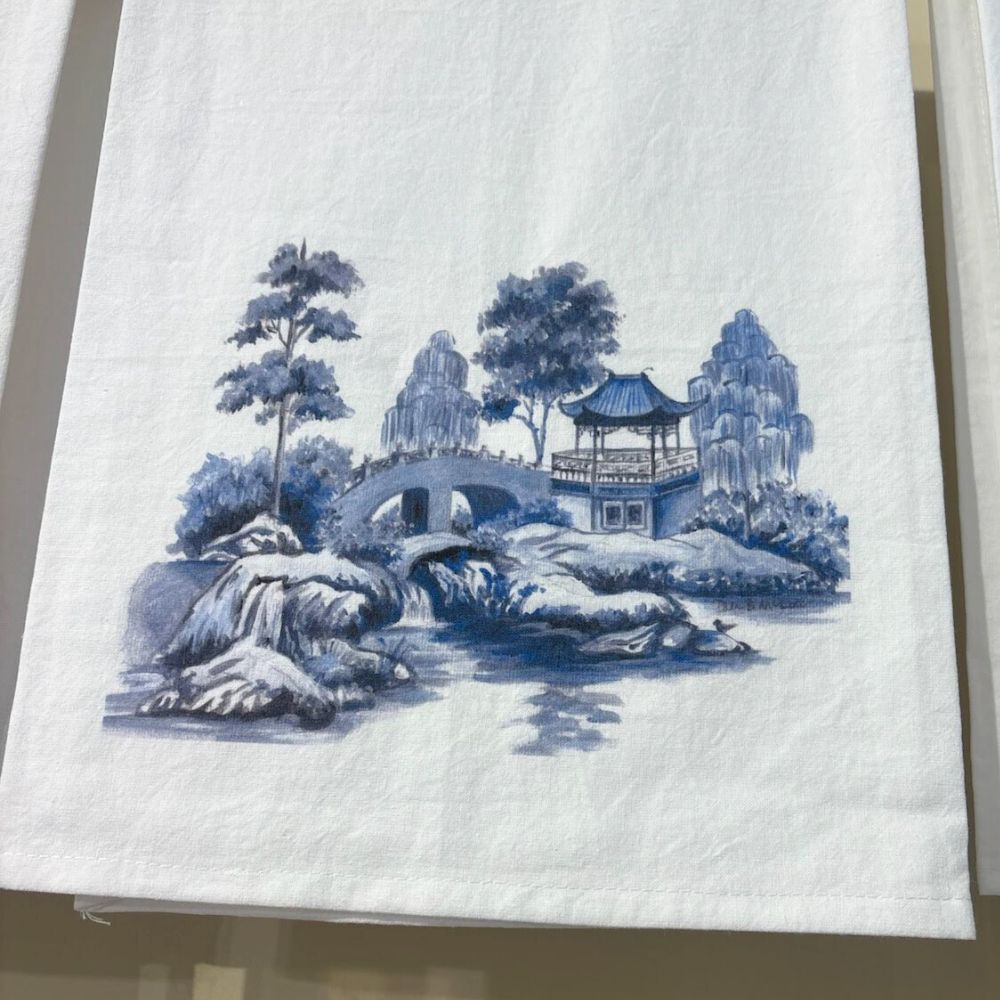 Blue and white chinoiserie-inspired tea towel featuring a serene landscape with a pagoda, arched stone bridge, and willow trees beside a flowing river.