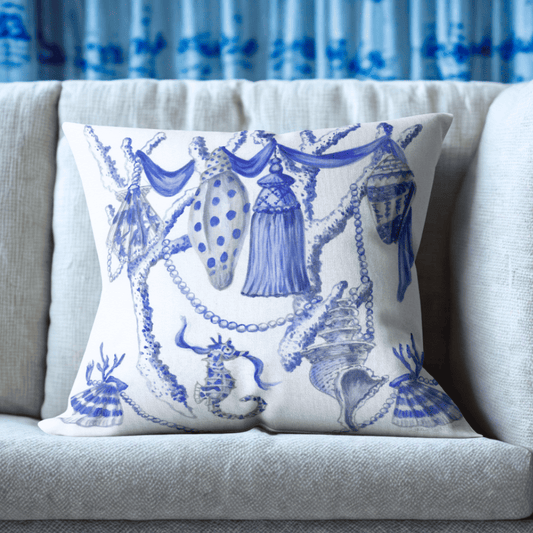 Blue and white chinoiserie-style pillow with seashells, tassels, pearls, coral, and a seahorse in a whimsical coastal design.