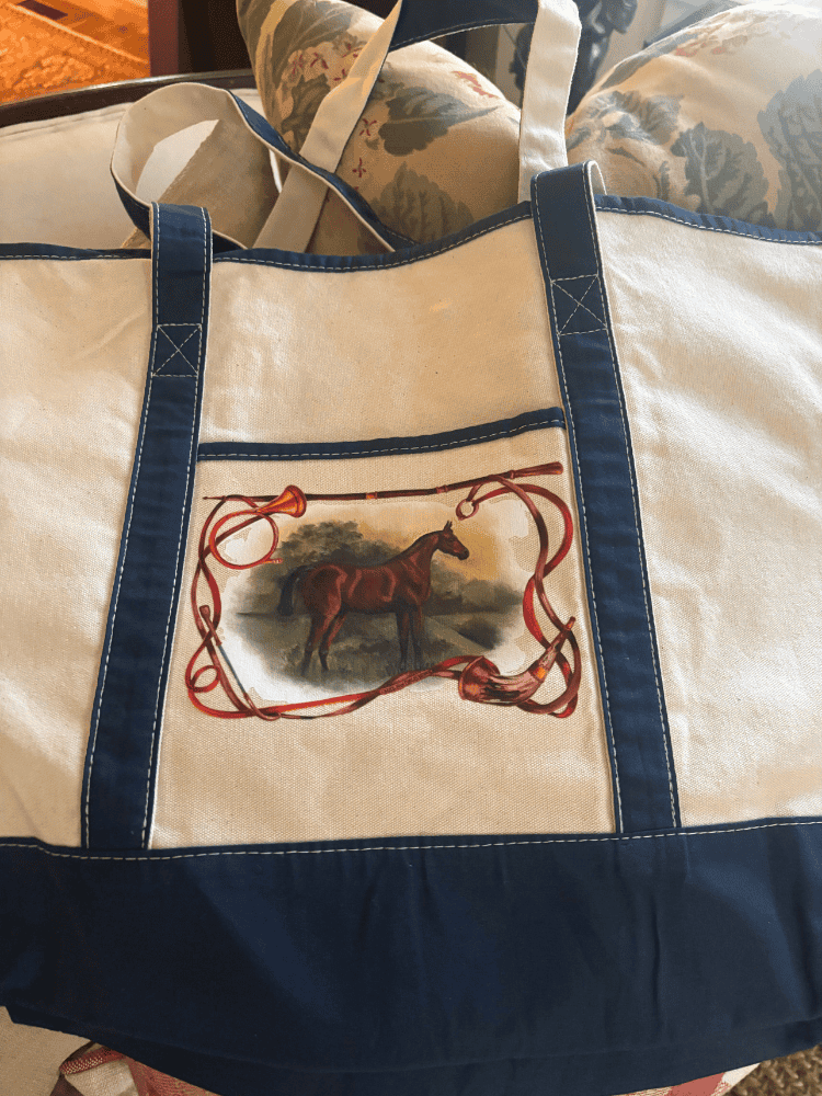 Canvas tote with navy trim and design of a chestnut horse standing in a field, framed by flowing reins and hunting horns.