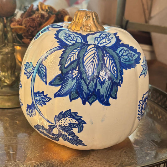 Hand-painted white pumpkin with intricate blue floral designs with a metallic gold stem, styled on a vintage silver tray.