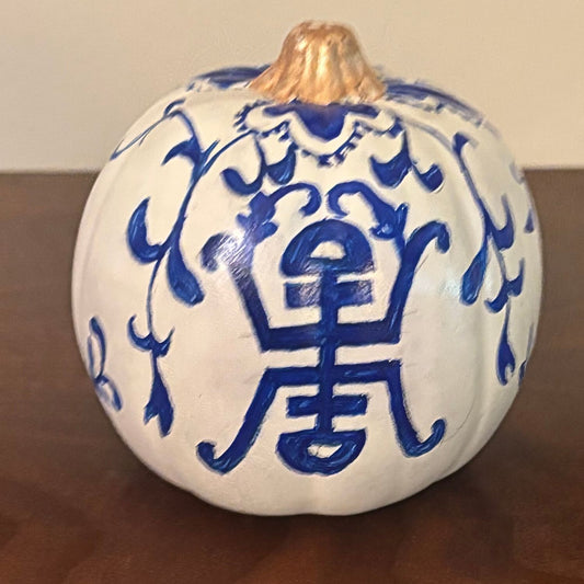 White hand-painted pumpkin with a cobalt blue symmetrical motif and vine-like flourishes, topped with a metallic gold stem.