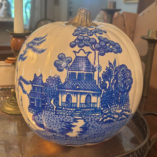 Front view of a hand-painted white pumpkin featuring a chinoiserie-style blue pagoda, floral trees, and birds, topped with a metallic gold stem.