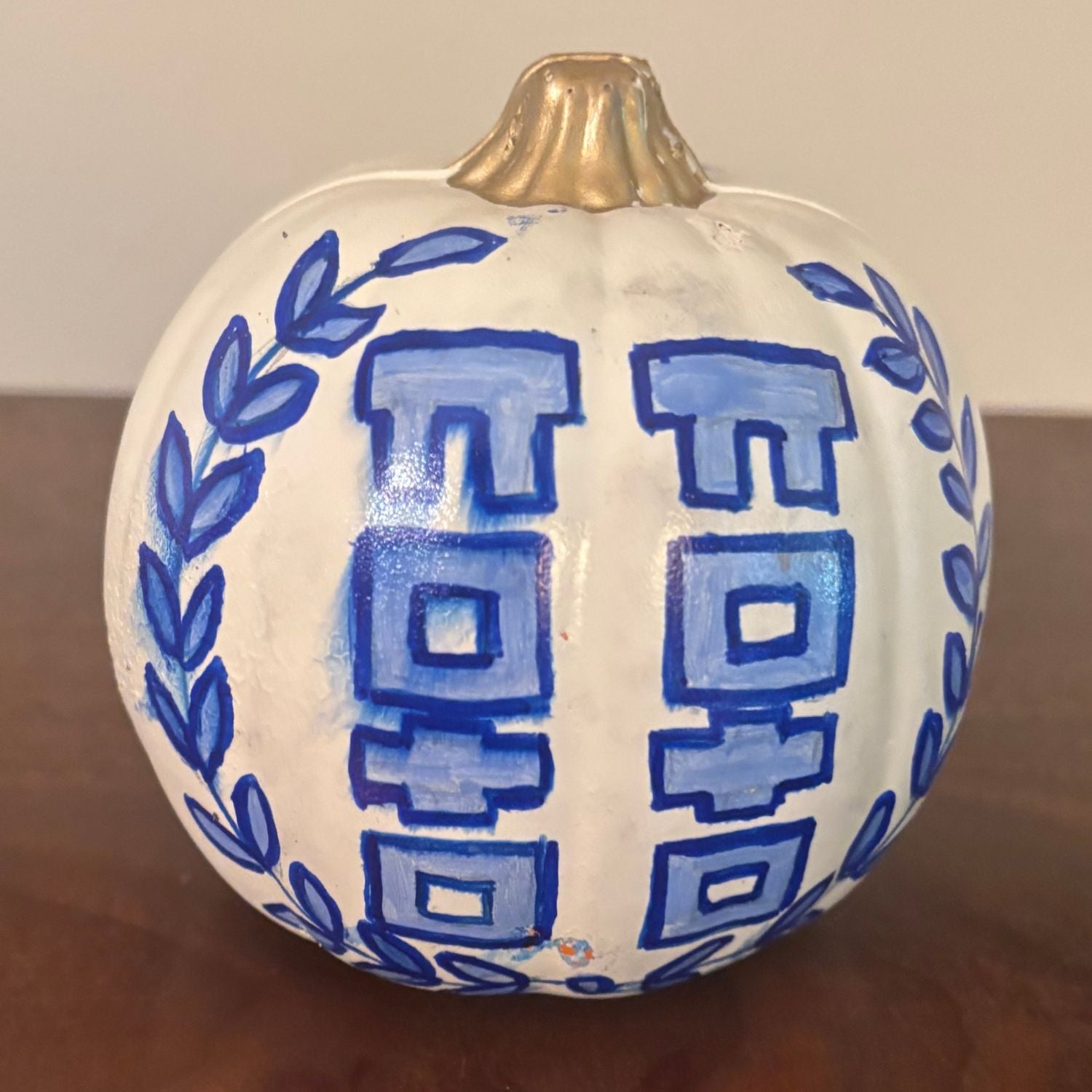 Hand painted white pumpkin with double blue block motif inspired by Chinese architectural forms, framed by blue leaf garlands and finished with a metallic gold stem.