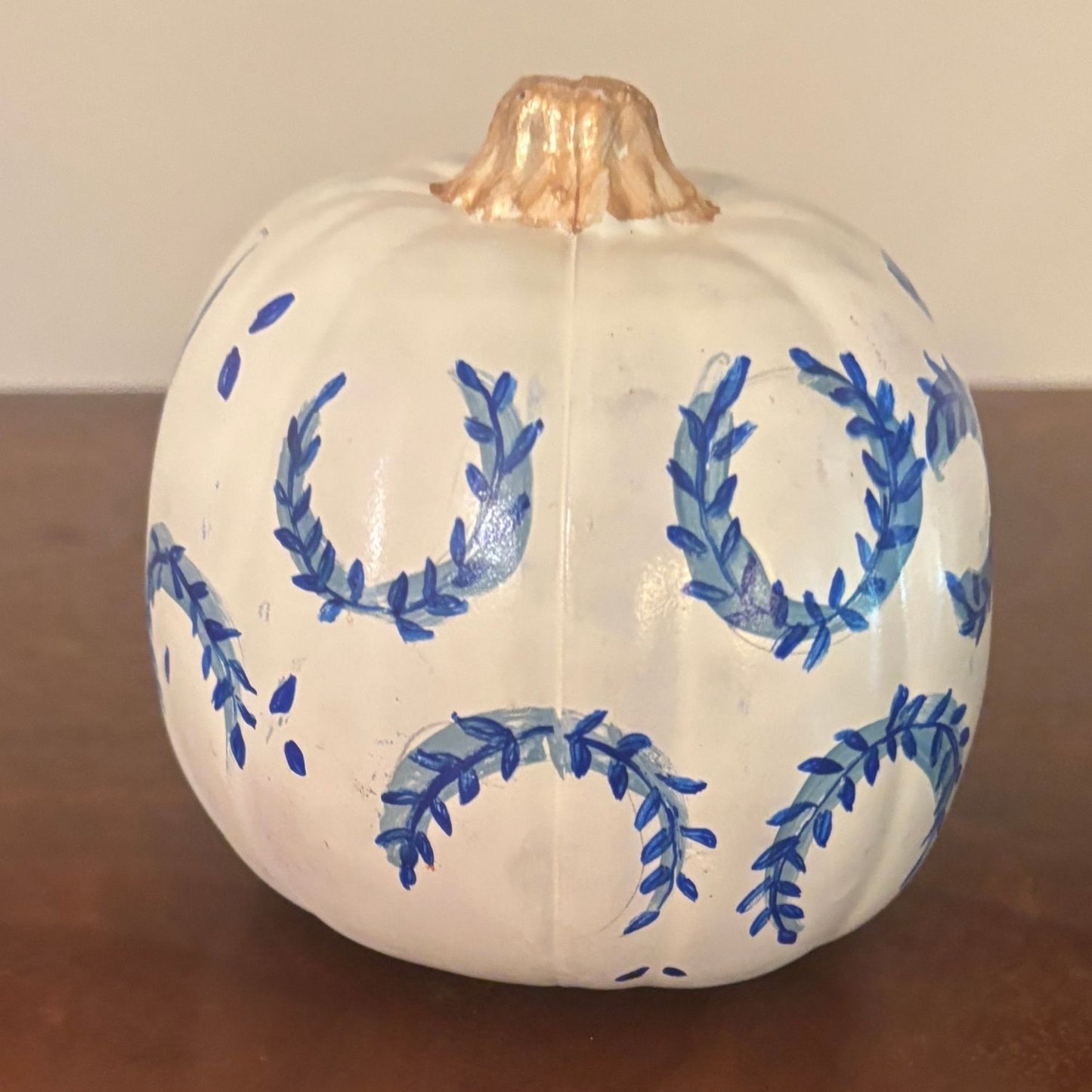 hand-painted decorative pumpkin showcasing a repeating laurel wreath pattern in cobalt blue