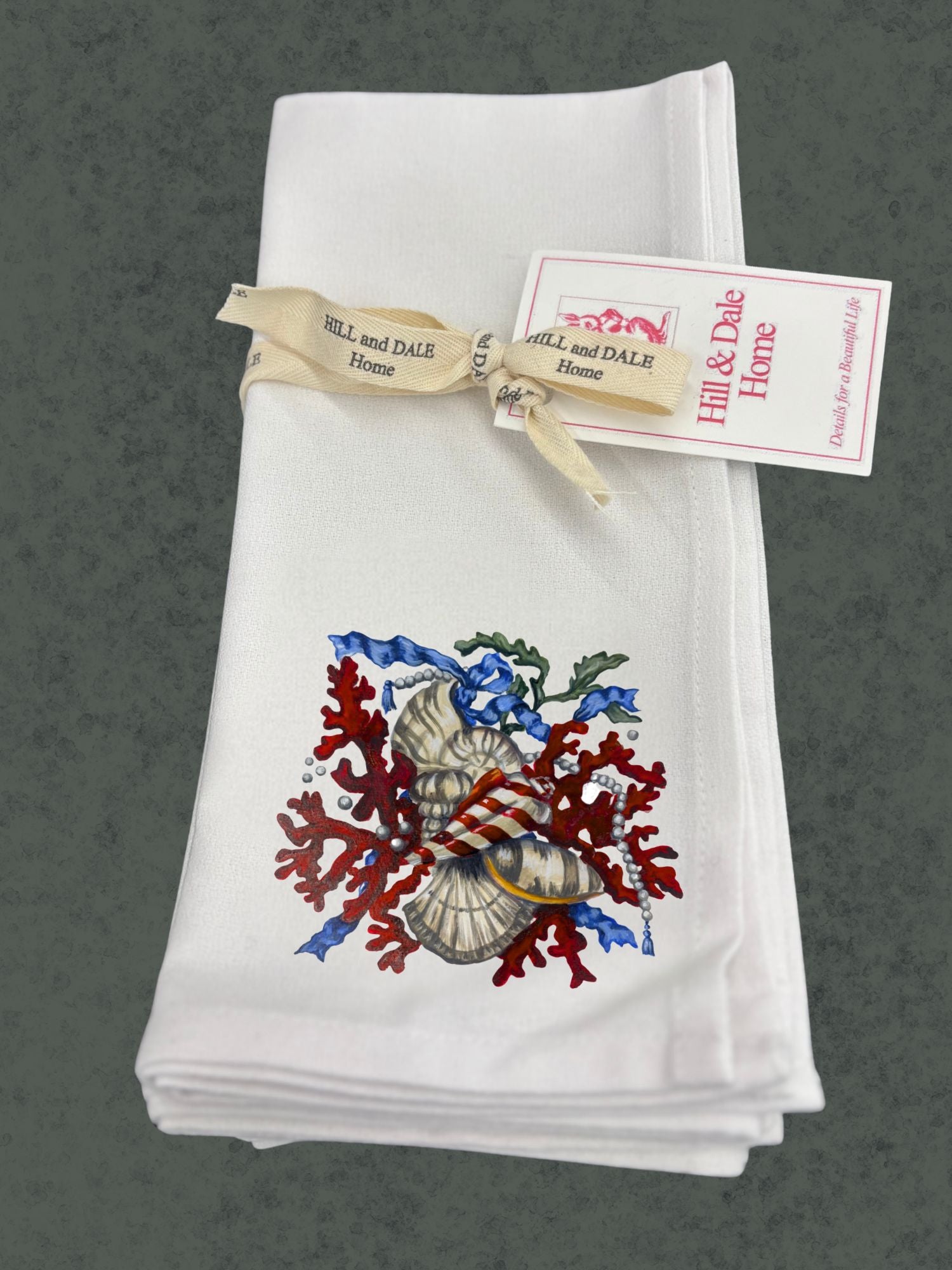Set of white Hill & Dale Home cloth napkins tied with branded ribbon, featuring Dale Barattini McLin artwork of red coral, seashells, pearls, and blue ribbon accents.