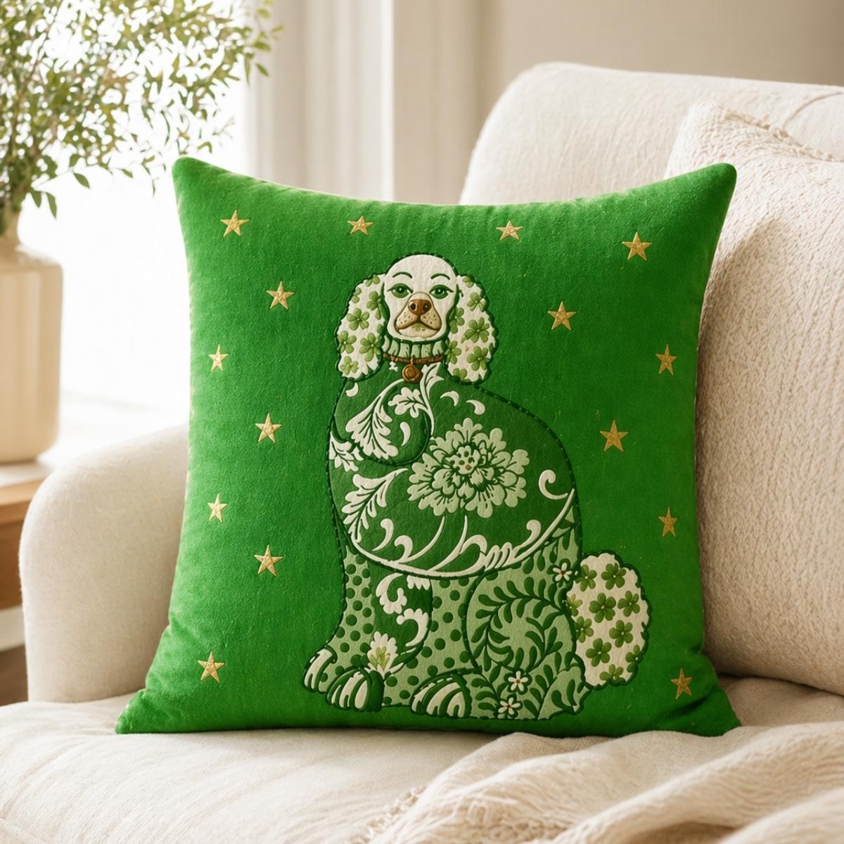 Green Staffordshire dog accent pillow with ornate floral details and gold stars, styled on a light upholstered chair with a cozy cream throw blanket.