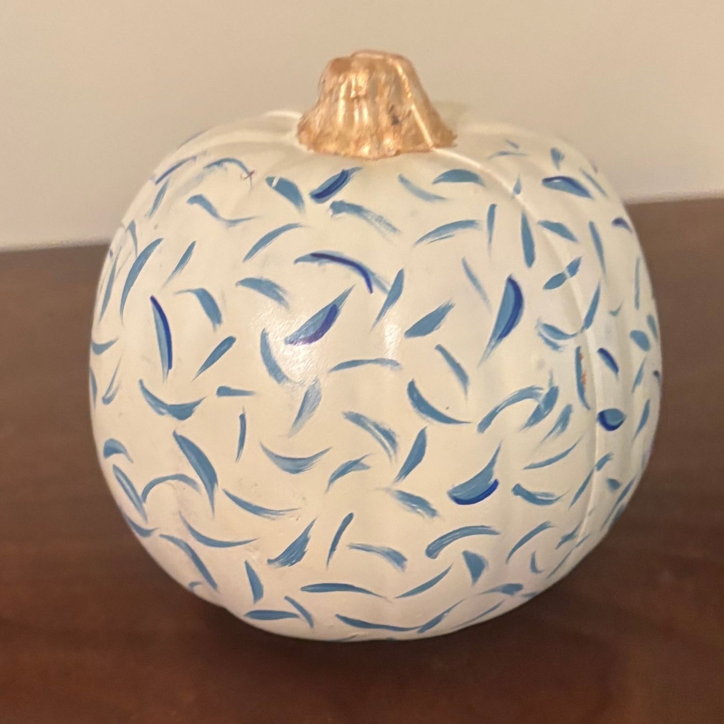 White pumpkin with swirling blue brushstroke pattern and gold-painted stem